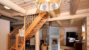 Un interior de madera con una escalera, una chimenea, un televisor y una zona de comedor.