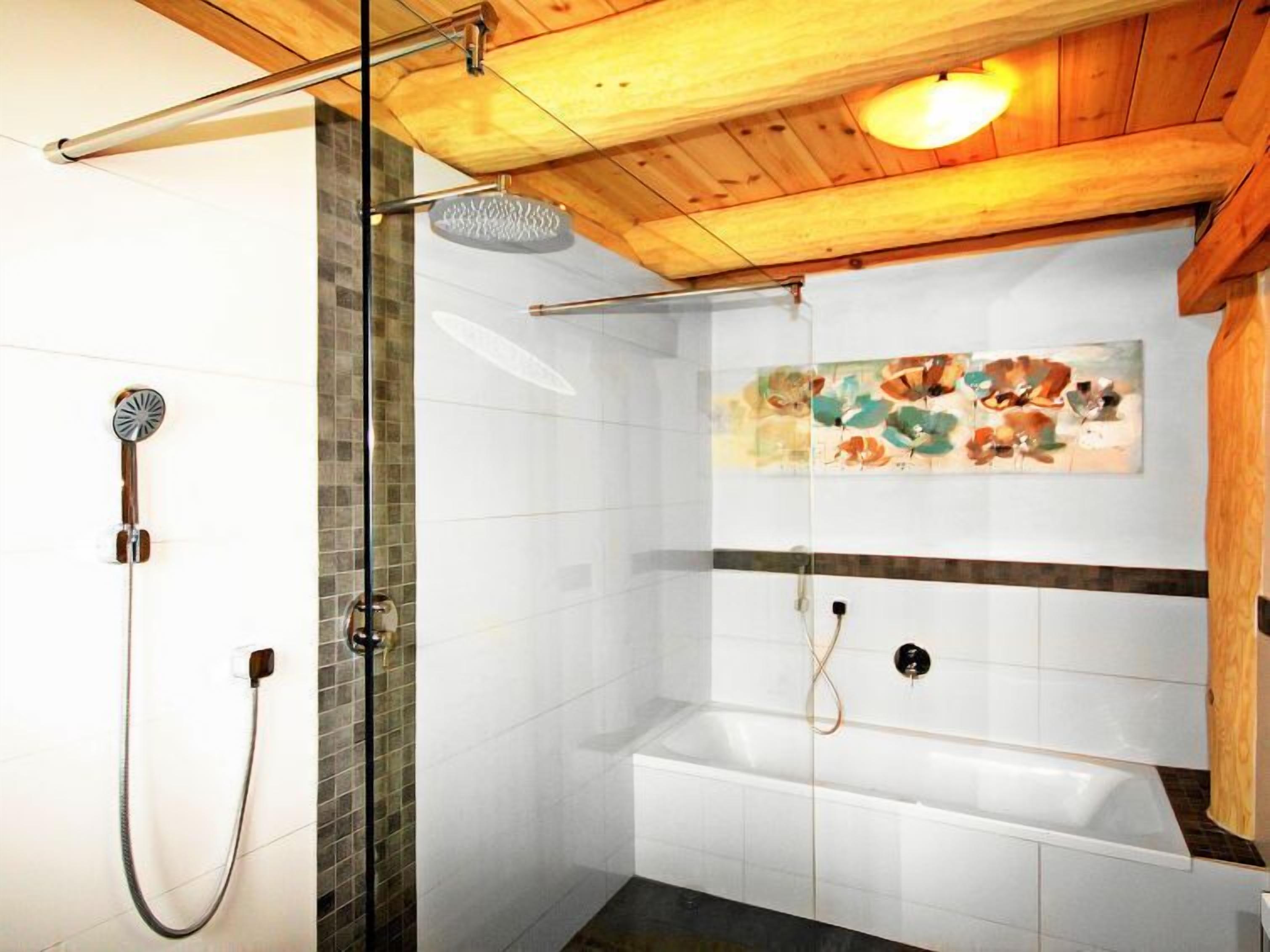 A modern bathroom with a glass shower enclosure, a bathtub, and a wooden ceiling.