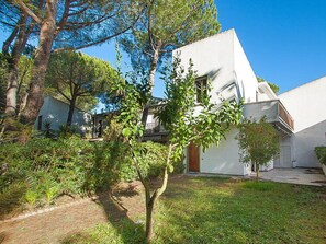 Una casa moderna con fachada blanca, rodeada de abundante follaje y árboles.