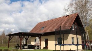 A two-story building with a red-tiled roof, a covered patio area with a table and chairs, and a small window.