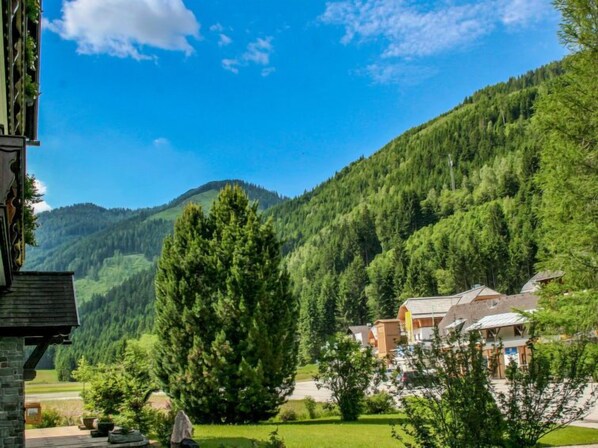 A mountain lodge with a stone facade, surrounded by lush greenery and a clear blue sky.