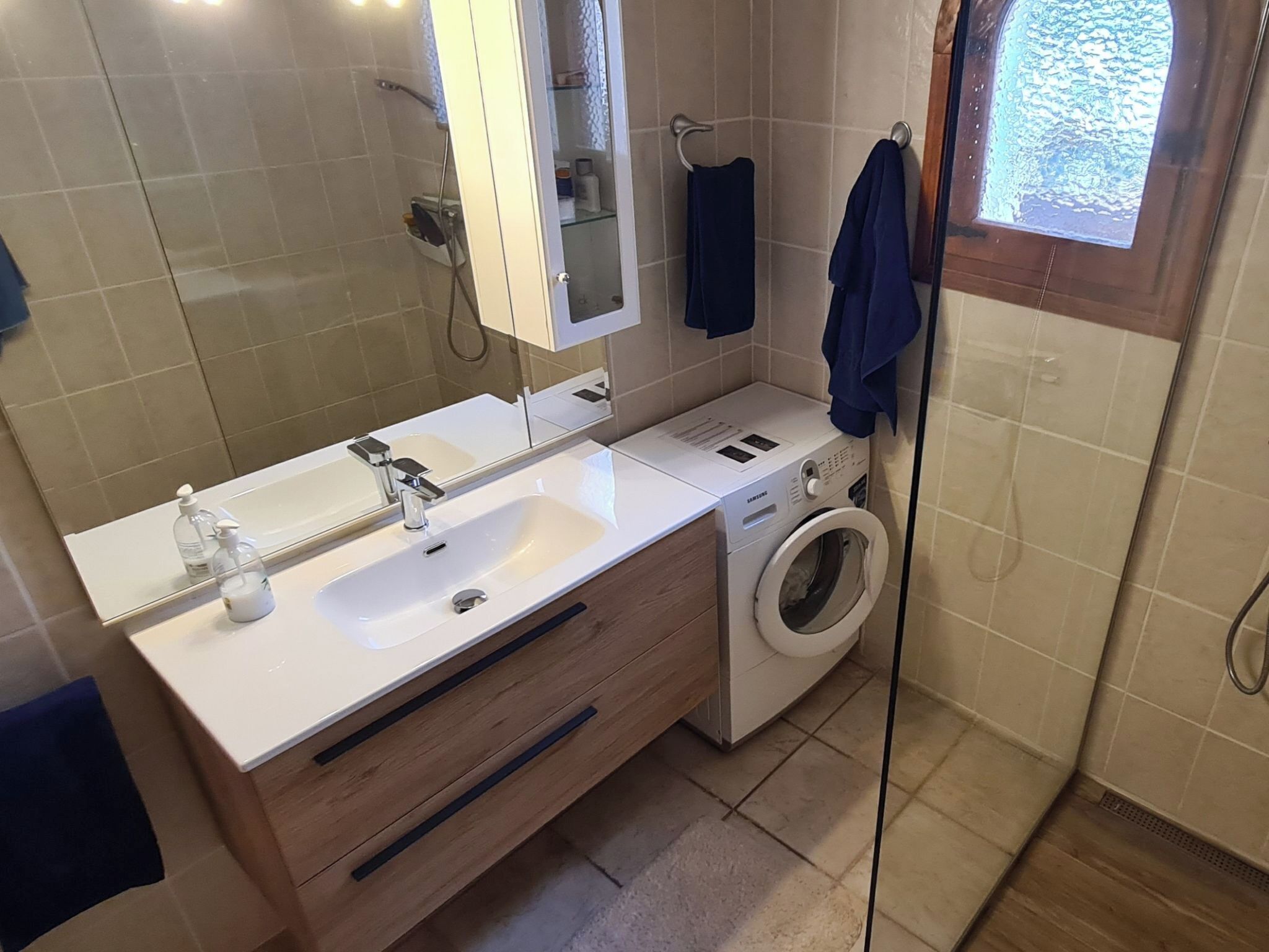 A modern bathroom with a double sink, a built-in washing machine, and a large mirror.