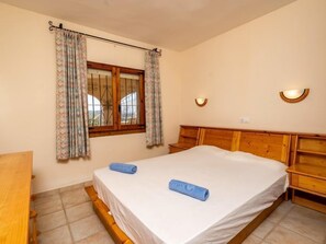Ein Schlafzimmer mit einem hölzernen Bett, einem Fenster mit Vorhängen, einem Nachttisch und einer Wandleuchte.