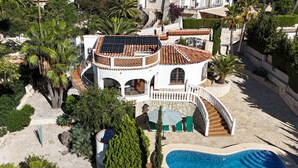 Une grande maison à plusieurs étages, dotée d’une piscine, entourée d’une végétation luxuriante et de palmiers.