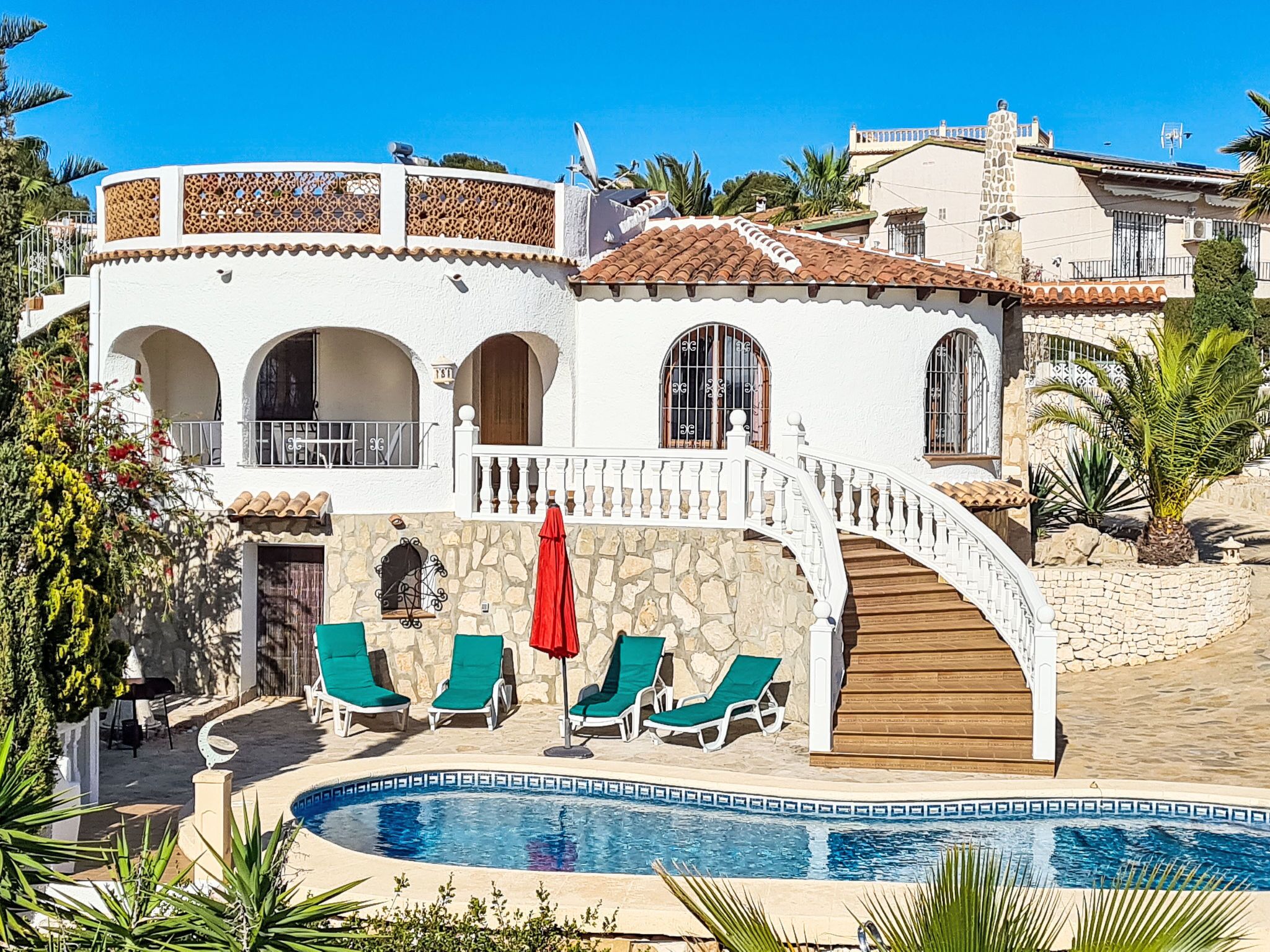 A two-story villa with a stone facade, a curved staircase, and a swimming pool.