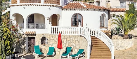 Una villa de dos plantas con fachada de piedra, una escalera curva y una piscina.