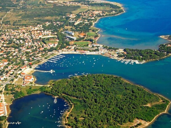 An aerial view of a coastal town with a marina, residential areas, and a forested peninsula.