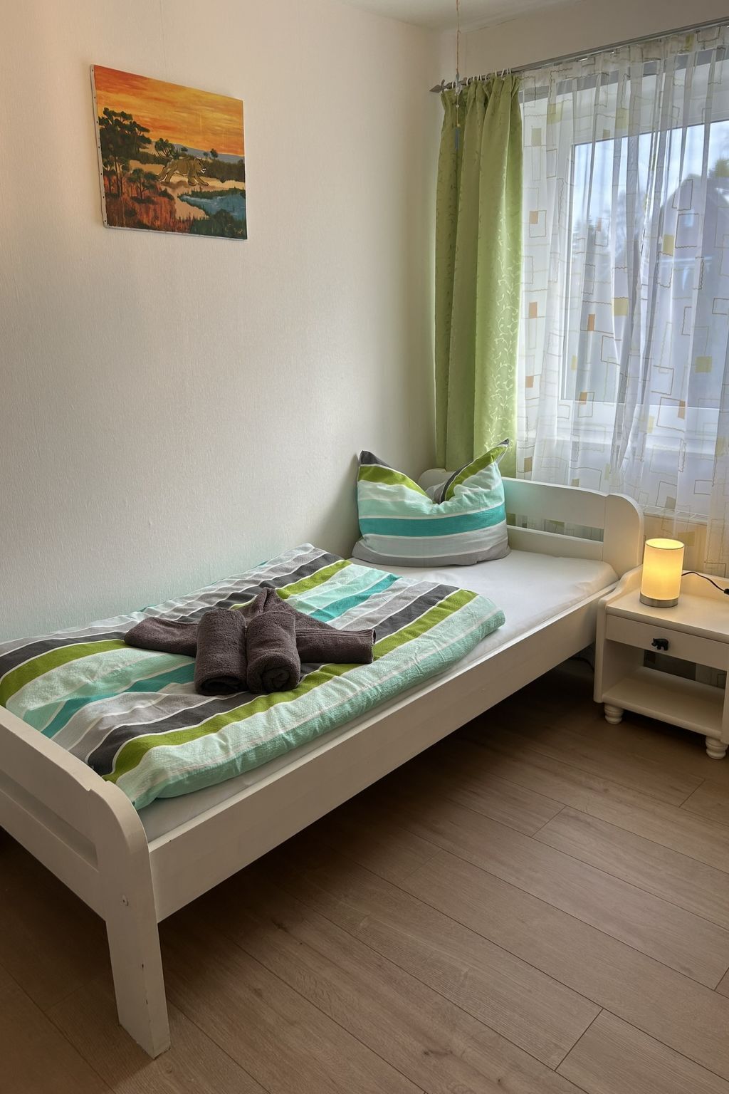 Ein Einzelbett mit gestreifter Decke, Kissen, einer Nachttischlampe und einem Bild an der Wand.