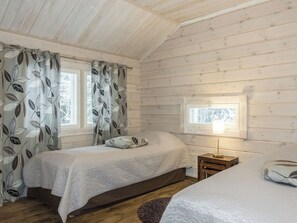 Ein gemütliches Schlafzimmer in einer Hütte mit zwei Betten, einem Fenster mit Aussicht und einer Nachttischlampe.