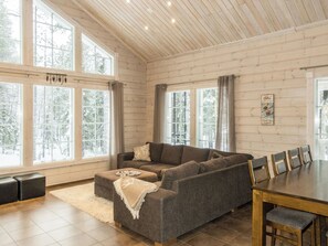 Una sala de estar acogedora con un sofá modular, una mesa de comedor con sillas y ventanas amplias que ofrecen vistas a árboles cubiertos de nieve.