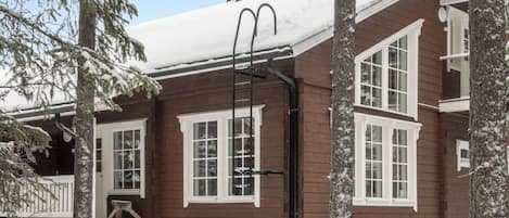 A wooden cabin with a snow-covered roof, large windows, and a chimney.