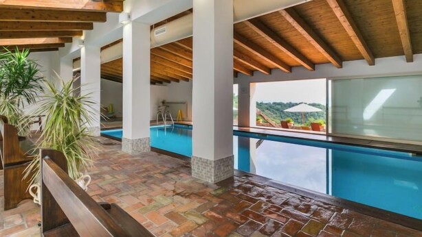 Un área de piscina techada con vistas al exterior, vigas de madera y suelo de baldosas.