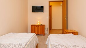 A bedroom with two beds, a TV, a bedside table with a lamp, and a wooden wardrobe. - Lakefront 2 by Interhome (Balatonlelle)