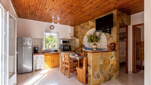 Une cuisine dotée d’un îlot central en pierre, d’un plafond en bois et offrant une vue sur la verdure environnante.