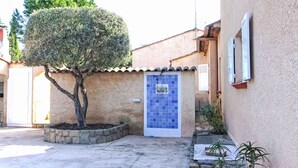 Une cour avec une porte carrelée, un arbre et un bâtiment à l’extérieur recouvert d’enduit.