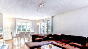 Un salon moderne avec un canapé d’angle, une table basse en verre et un coin repas comprenant des chaises et une table.
