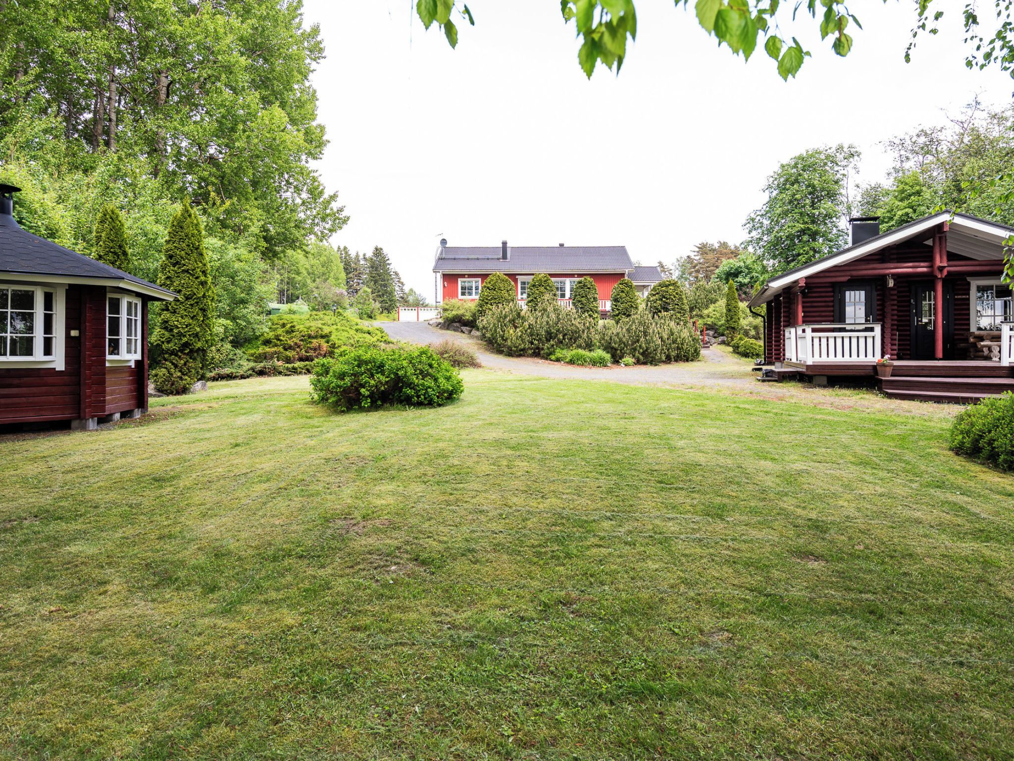 A residential property with a well-maintained lawn, a red house, and a wooden cabin.