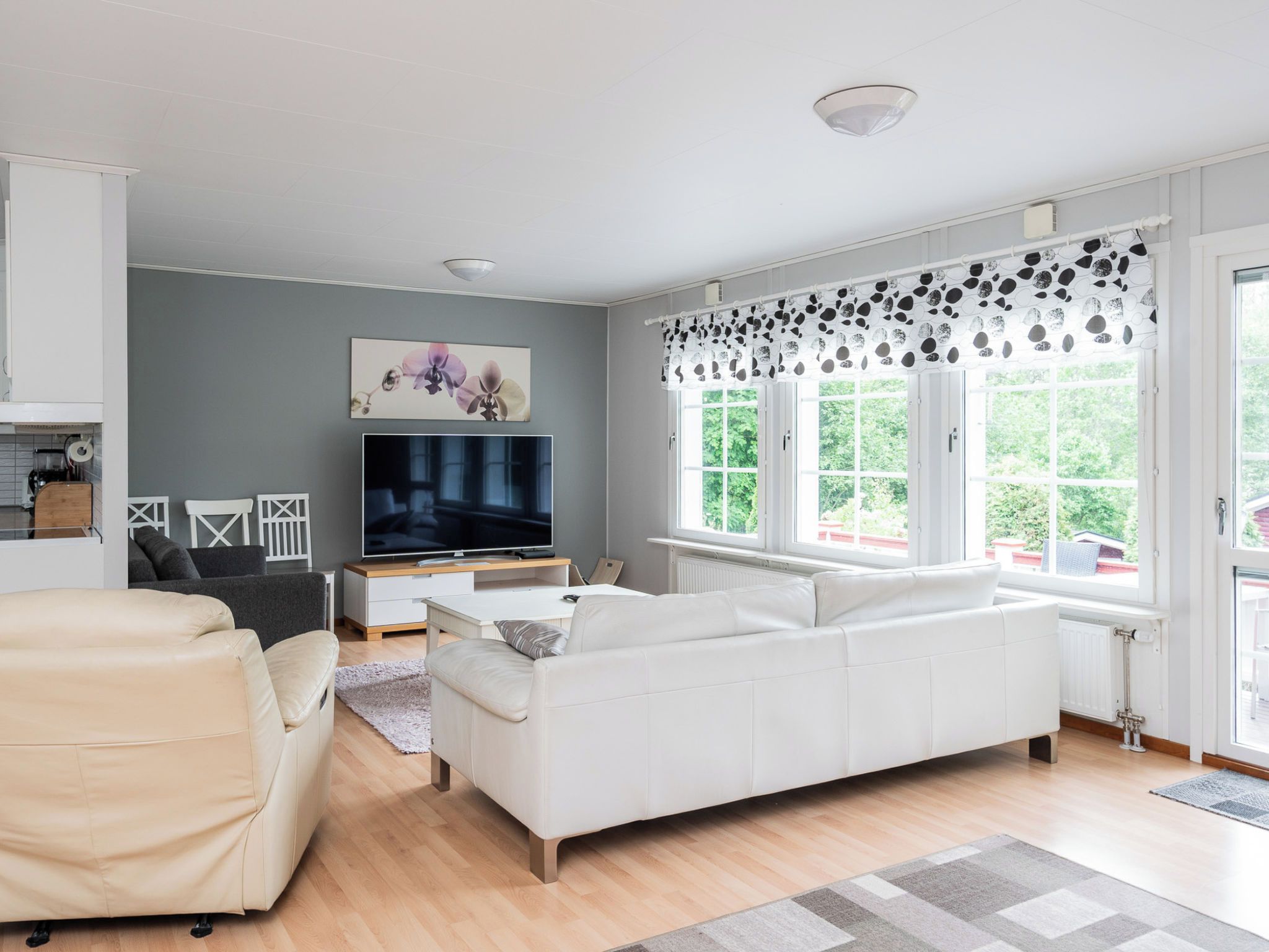 A modern living room with a white sofa, a television, and a large window with patterned curtains.