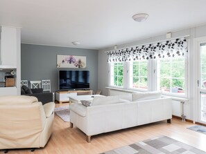 A modern living room with a white sofa, a television, and a large window with patterned curtains.