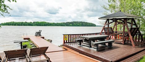 A wooden deck with picnic tables and benches, overlooking a calm lake with a forested shoreline.