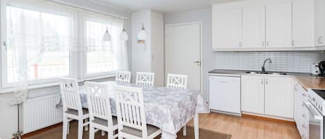 A modern kitchen with white cabinetry, a dining table with chairs, and a view of the outside through large windows.