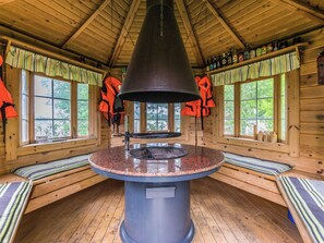 L’intérieur d’une cabane est agrémenté d’une cheminée en pierre au centre, de murs en bois et de fenêtres avec des rideaux.