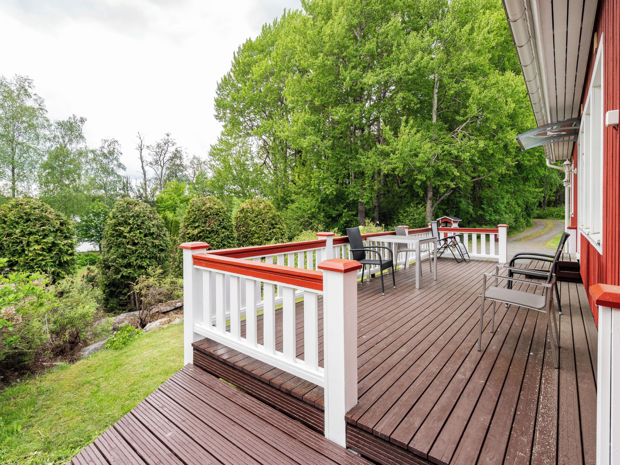 Une terrasse en bois avec des meubles d’extérieur, une balustrade blanche et un bâtiment rouge en arrière-plan.