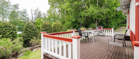 A wooden deck with outdoor furniture, a white railing, and a red building in the background.