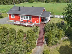 Una casa roja con porche y terraza, rodeada de un césped cuidado y árboles.
