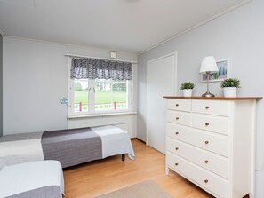 A bedroom with two beds, a dresser, a window with curtains, and a view of a green landscape. - Käpälämäki by Interhome (Somero)
