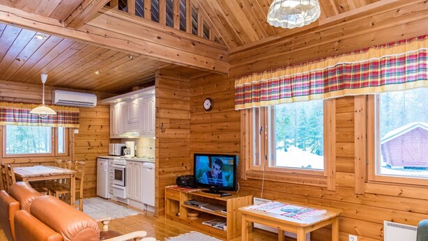 A cozy cabin interior with wooden walls, a dining area, a living room with a television, and a kitchen.