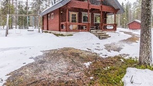 A rustic cabin with a porch, surrounded by snow-covered ground and trees.