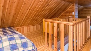 A wooden cabin interior with a bed, a wooden staircase, and a sloped ceiling.