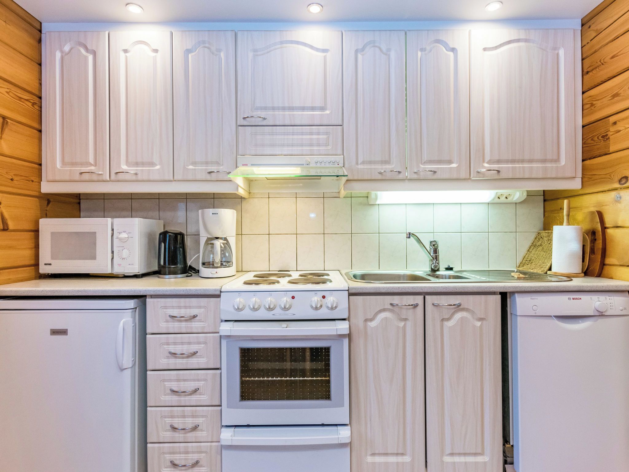 A compact kitchen with white cabinetry, a Bosch coffee maker, a microwave, a stove, and a dishwasher.