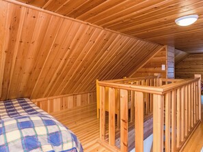 A wooden interior with a sloped ceiling, a bed with a plaid blanket, and a wooden railing. - Revontuli by Interhome (Kuusamo)