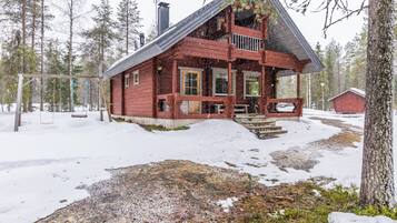 Punainen puinen mökki, jossa on kuisti, ja sen ympärillä on lunta ja puita.