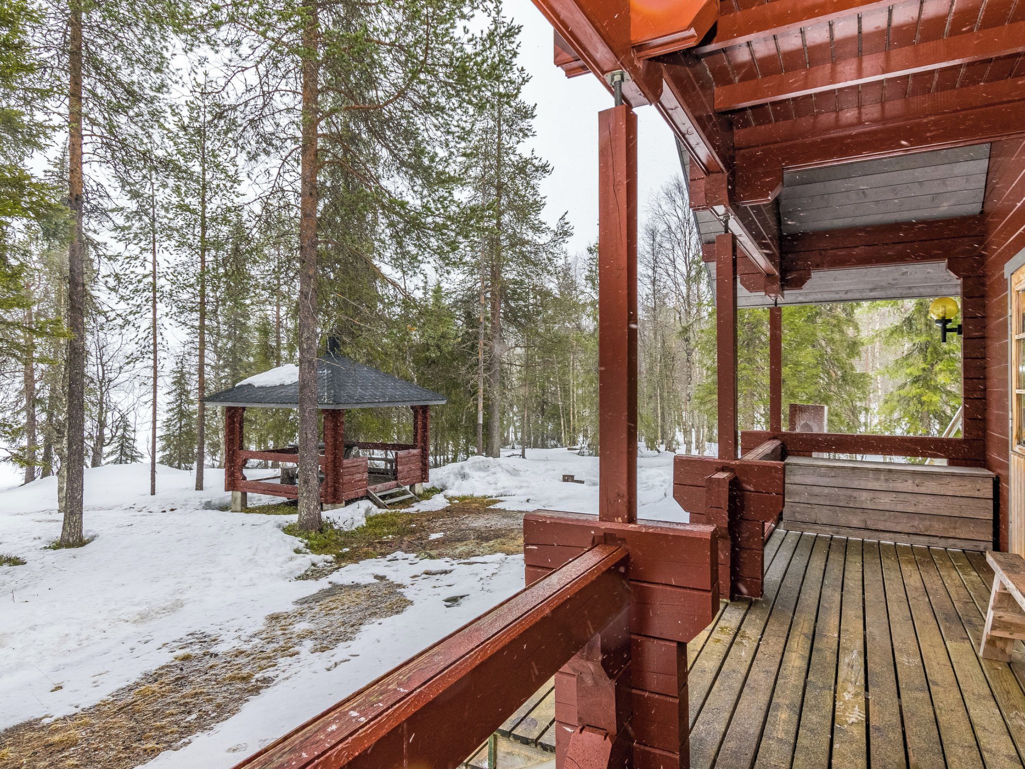 Una casetta di legno con veranda e un piccolo gazebo in una foresta innevata.