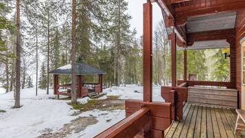 Una casetta di legno con veranda e un piccolo gazebo in una foresta innevata.