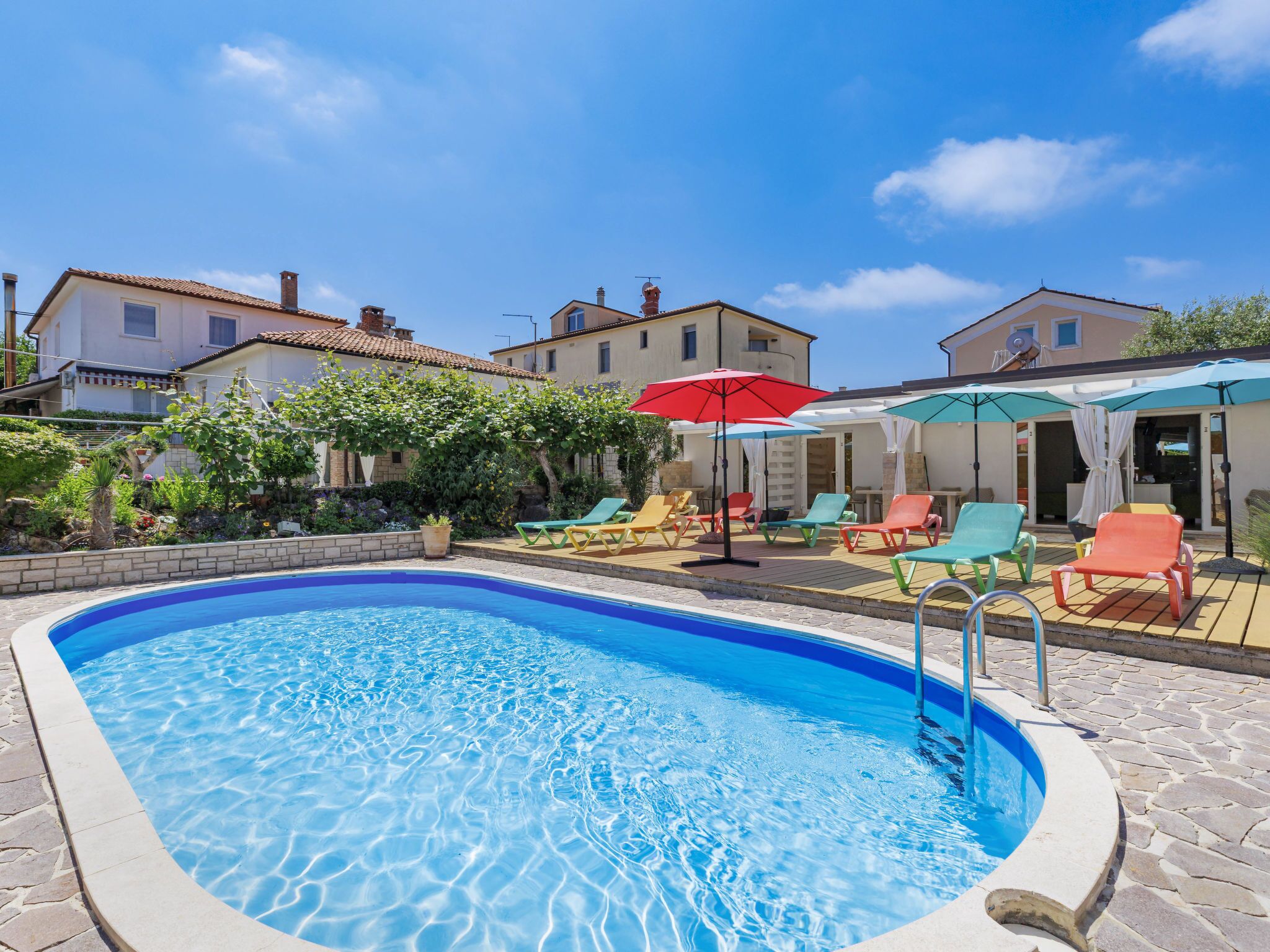 A swimming pool with lounge chairs and umbrellas, surrounded by buildings and greenery.