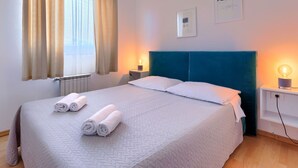 Un lit bien fait, avec des serviettes pliées, une tête de lit bleue, des lampes de chevet et une fenêtre avec des rideaux.