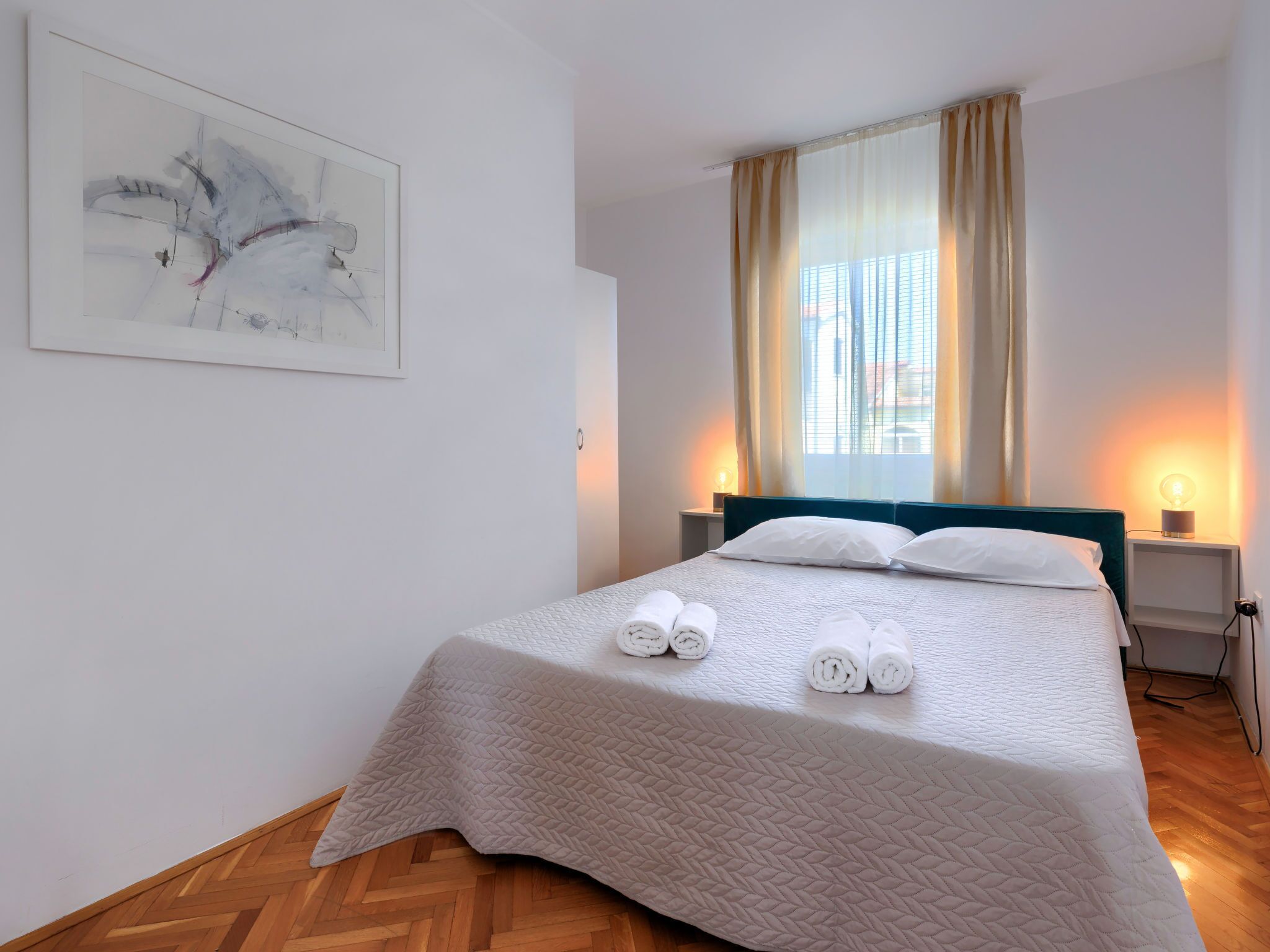 A neatly made bed with rolled towels, a bedside lamp, and a window with curtains.