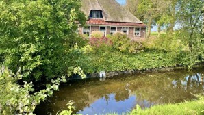 Une maison traditionnelle à toit de chaume, entourée d’une végétation luxuriante et bordée d’un plan d’eau paisible.