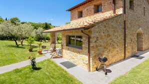Una casa de pedra amb teulada de rajola, una finestra i una barbacoa al pati.