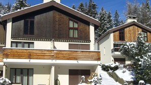 Een houten huis met twee verdiepingen en een balkon, omringd door met sneeuw bedekte bomen.