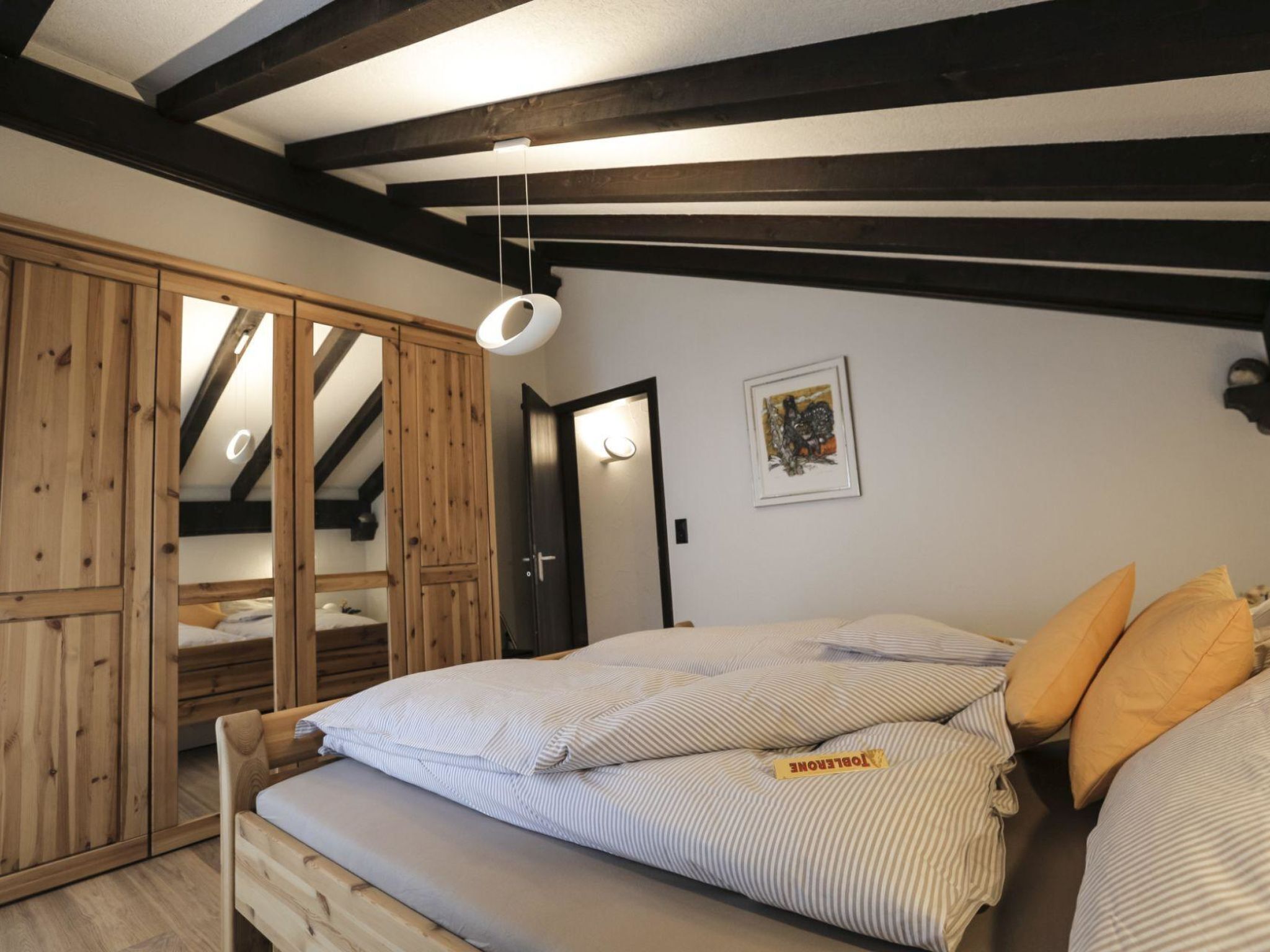 A bedroom with a bed, wooden wardrobe, and a ceiling with exposed beams.