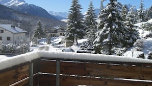 Een houten terras met een sneeuwbedekte balustrade, uitzicht op een bergketen en sneeuwzware bomen.