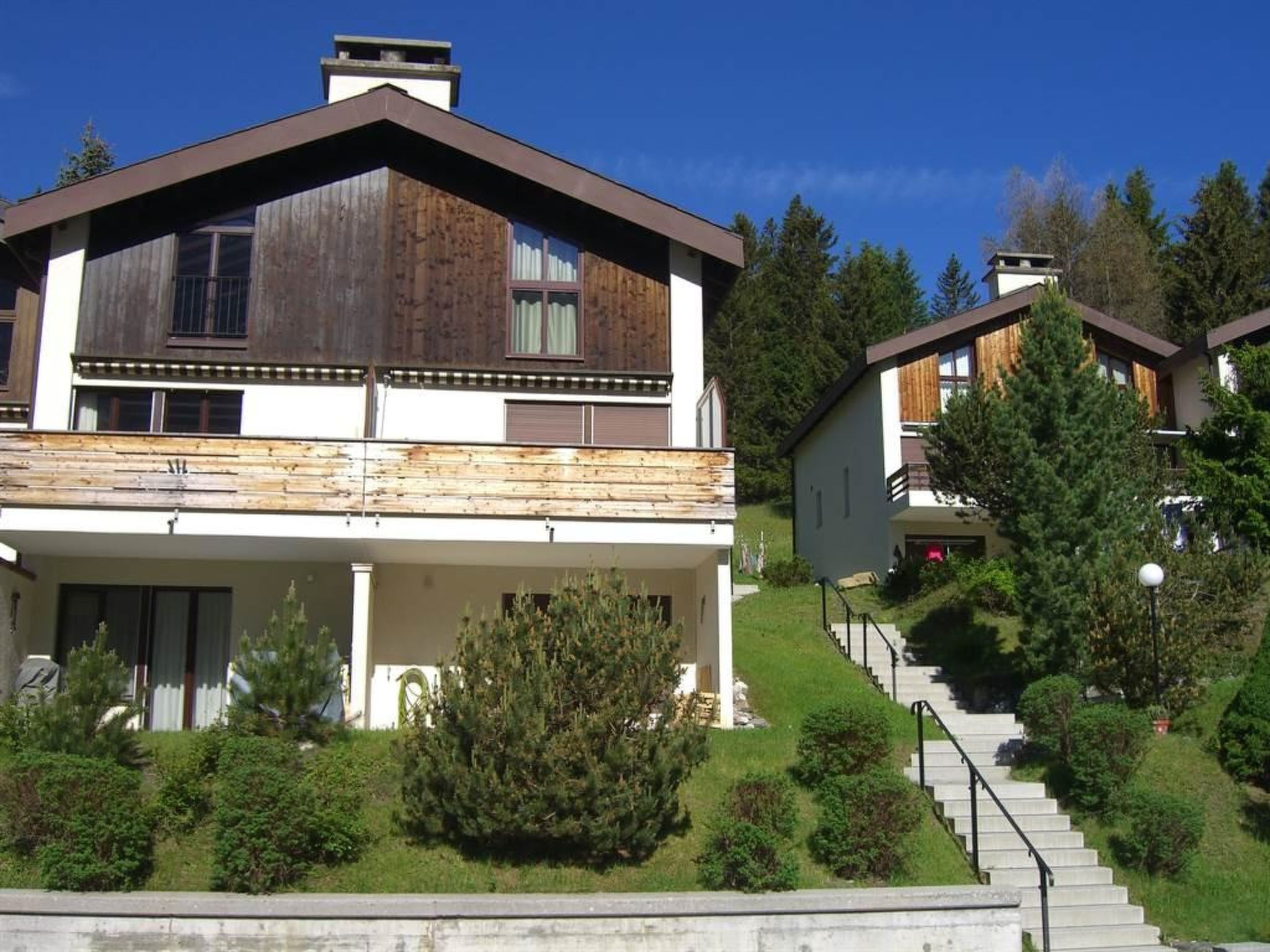 A modern two-story house with a wooden facade, a balcony, and a staircase leading to the upper floor.