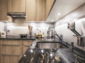 Een moderne keuken met houten kastjes, een zwarte marmeren aanrecht, roestvrijstalen apparatuur en een ingebouwd spoelbak.