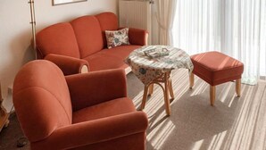 Een woonkamer met een bank, een ronde tafel met een tafelkleed met patroon, en een bijpassend voetenbankje.