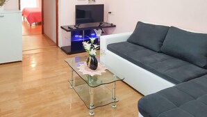 Een moderne woonkamer met een bank, een glazen salontafel met een vaas, een televisie op een meubelstuk en een gang die leidt naar een slaapkamer.